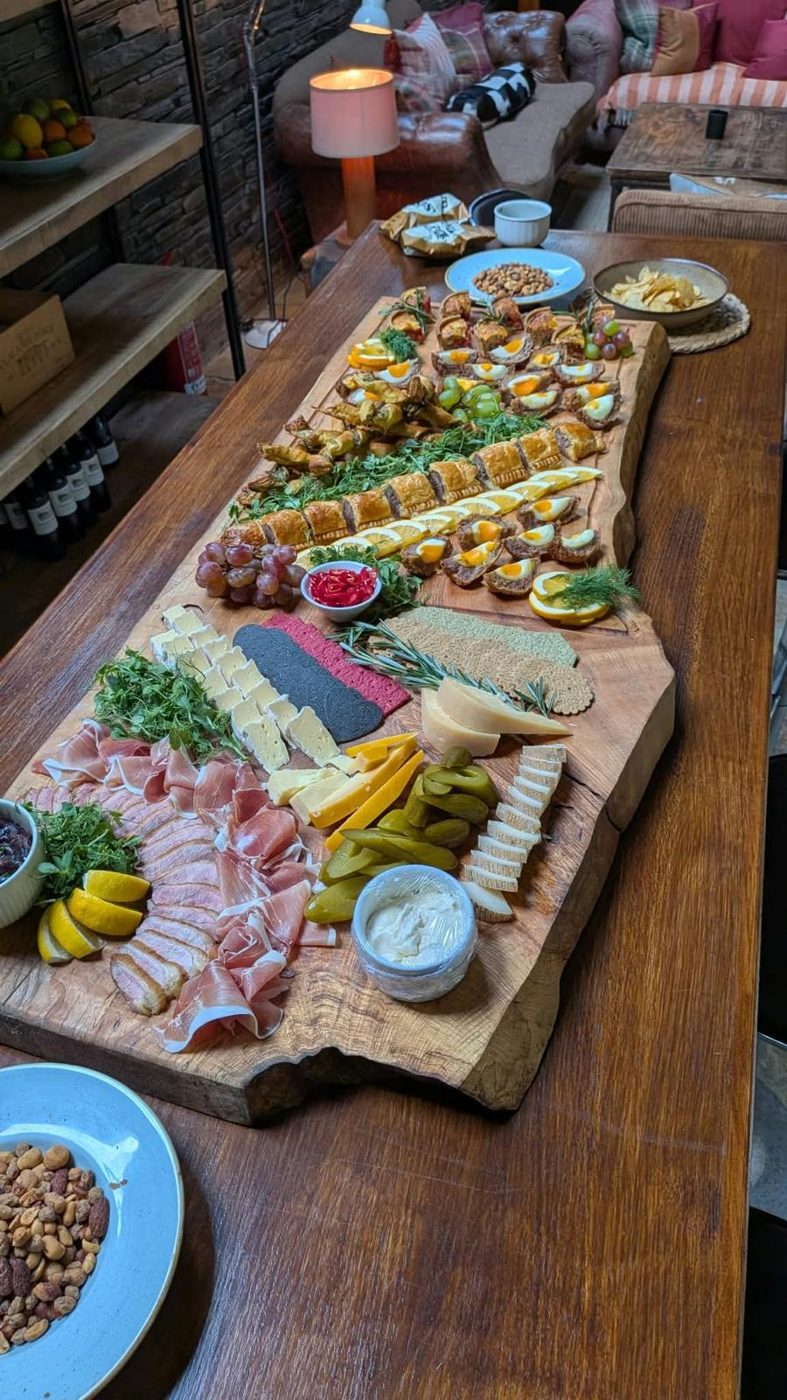 A long live-edge ash serving board laid with charcuterie, cheese, sausage rolls, Scotch eggs and quiche