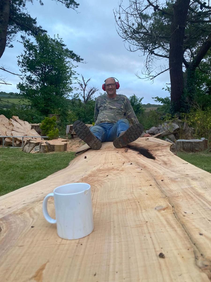 Peter sitting on a freshly milled Western red cedar slab with a mug of tea