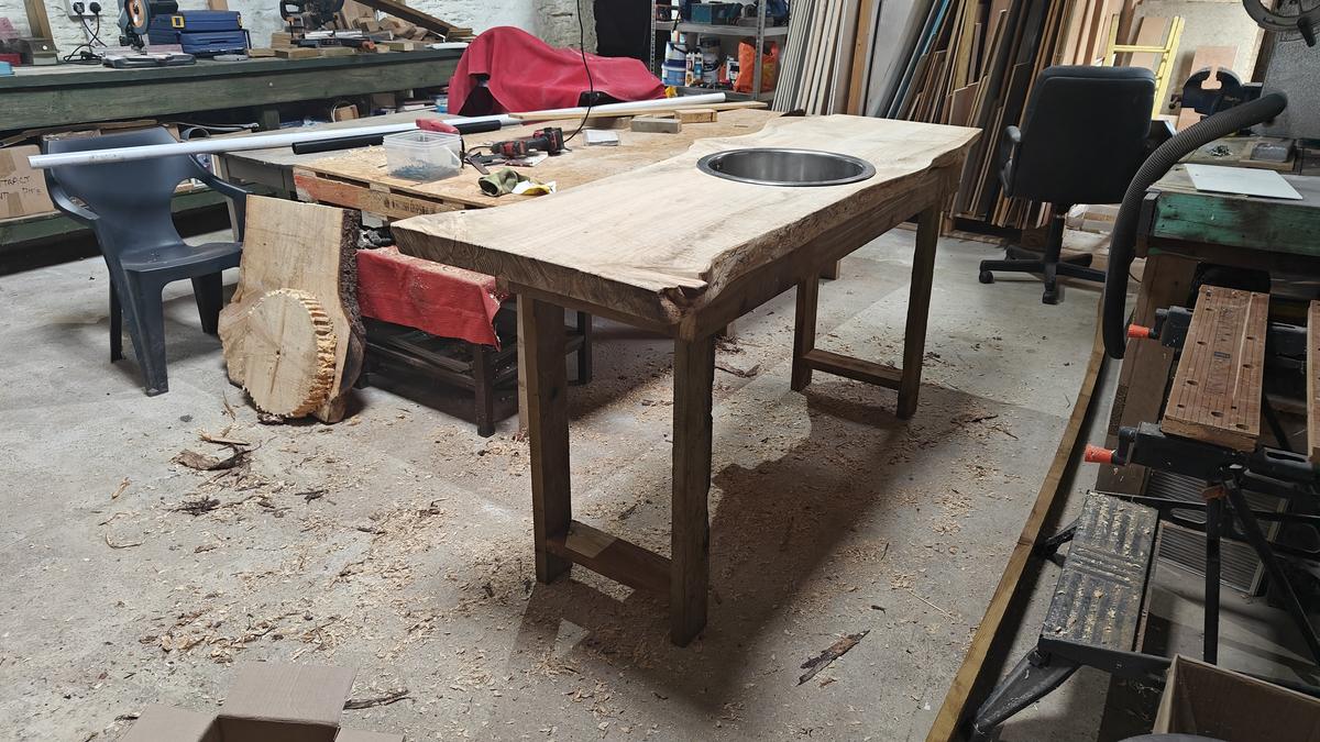 A live-edge glamping worktop on a timber frame with an inlaid round steel sink